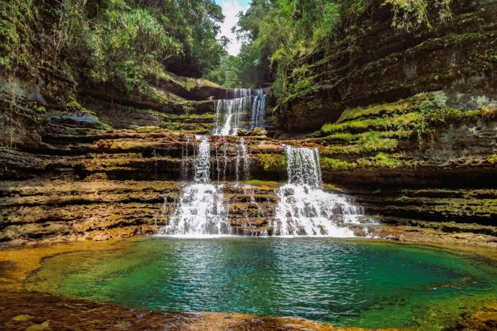 The three-tier Wei Sawdong Waterfall in Meghalaya, with clear turquoise water falling through rock layers and dense green forests around it